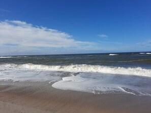 A beach with waves approaching the shore, clear sky, and distant horizon.