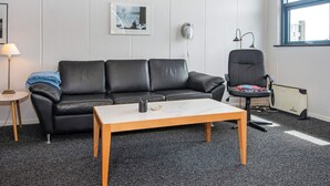 A modern living room with a black leather sofa, a wooden coffee table, a black office chair, a lamp, and a framed picture on the wall. - 6 Person Holiday Home in Hvide Sande (Hvide Sande)