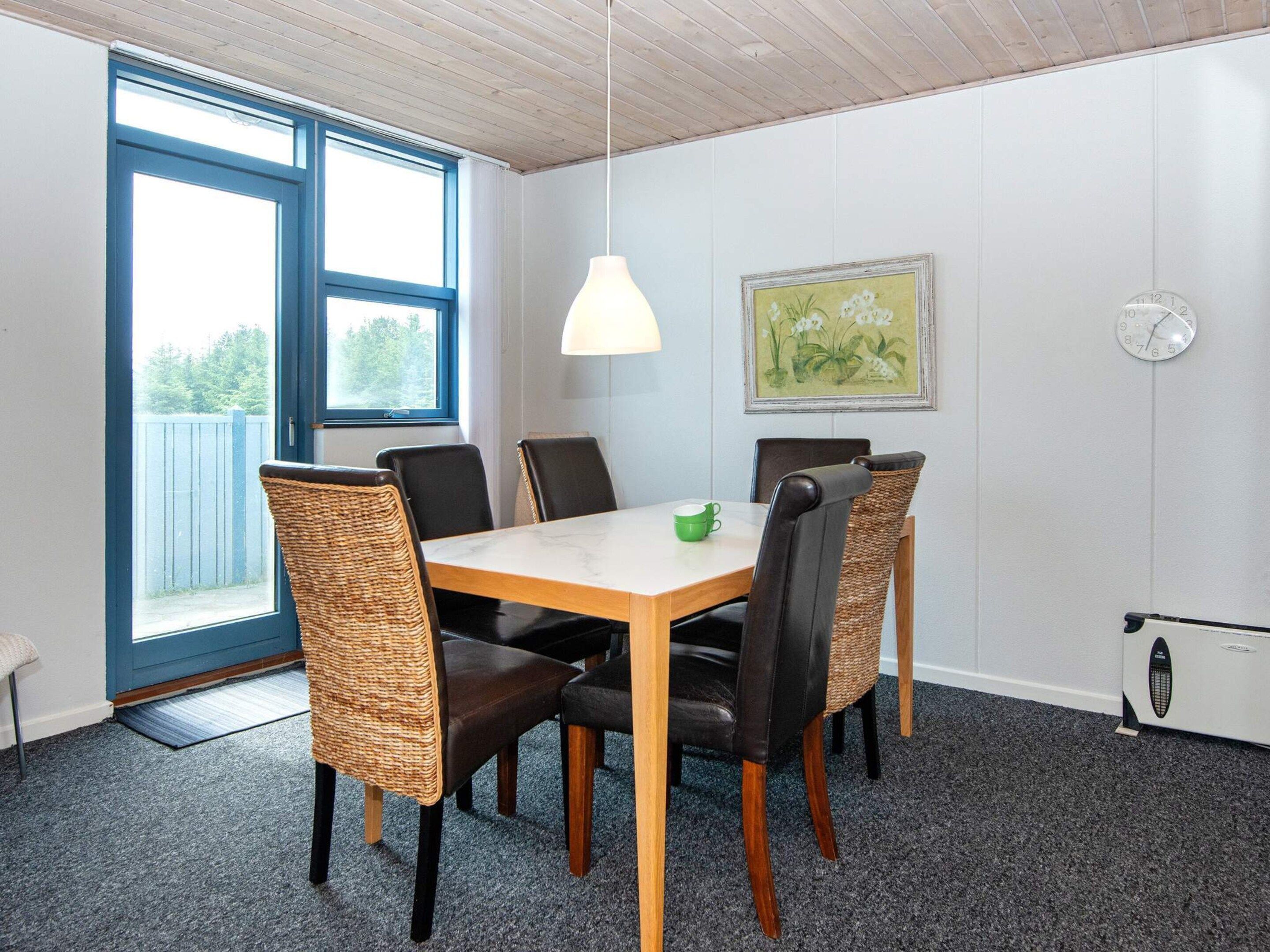 A dining area with a table, chairs, a hanging light, a clock, and a window.