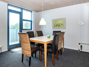 A dining area with a table, chairs, a hanging light, a clock, and a window. - 6 Person Holiday Home in Hvide Sande (Hvide Sande)