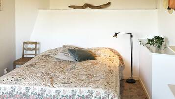 A bedroom with a bed, a chair, a desk, a lamp, and a plant.