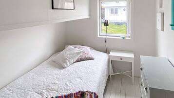 A single-bed room with a window, a bedside table, and a wardrobe.