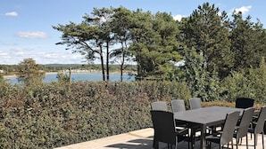 Eine Terrasse im Freien mit Tisch und Stühlen, mit Blick auf ein Gewässer und Bäume.