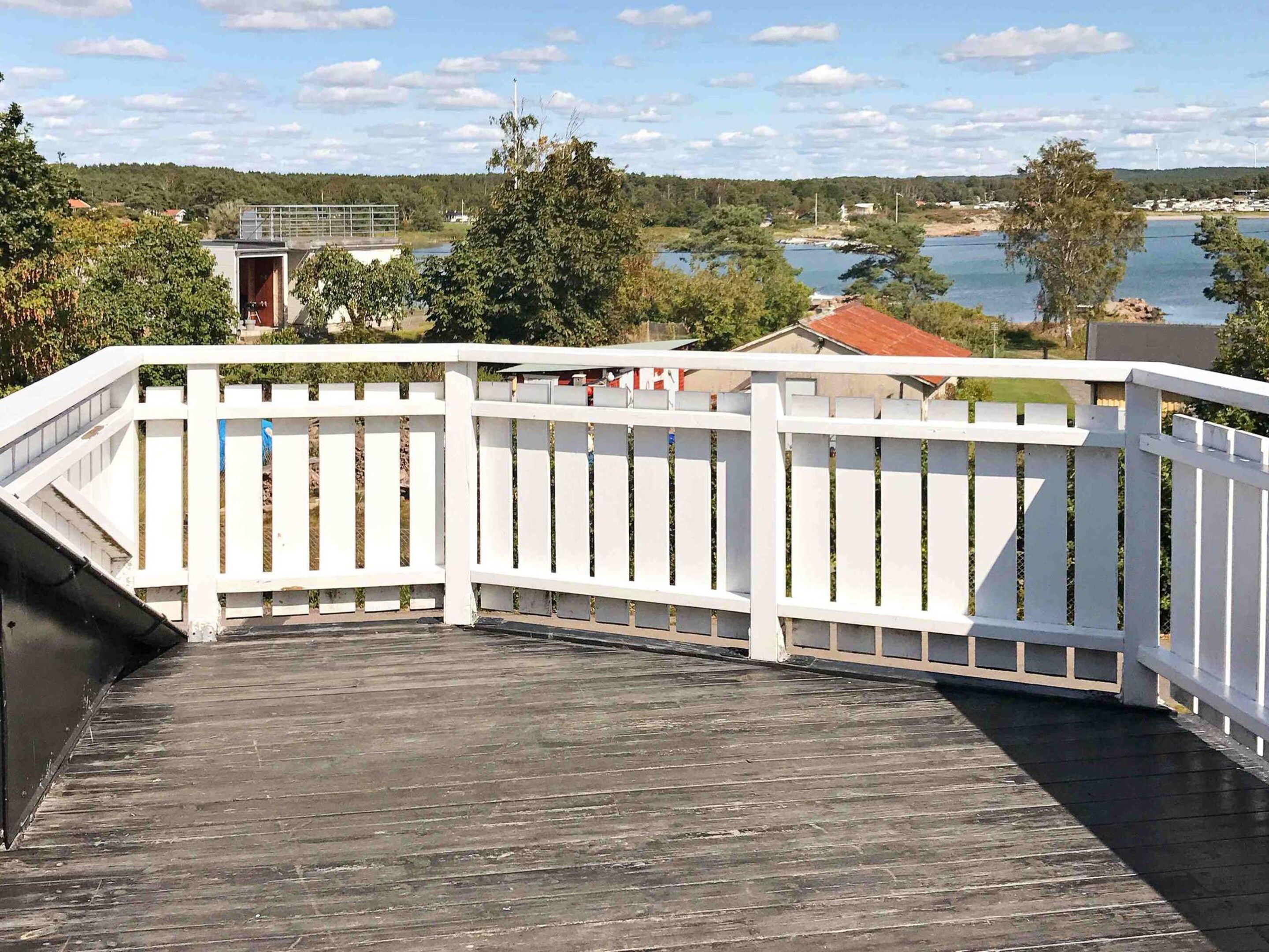 A wooden deck with a white railing overlooking a body of water and a forested area.