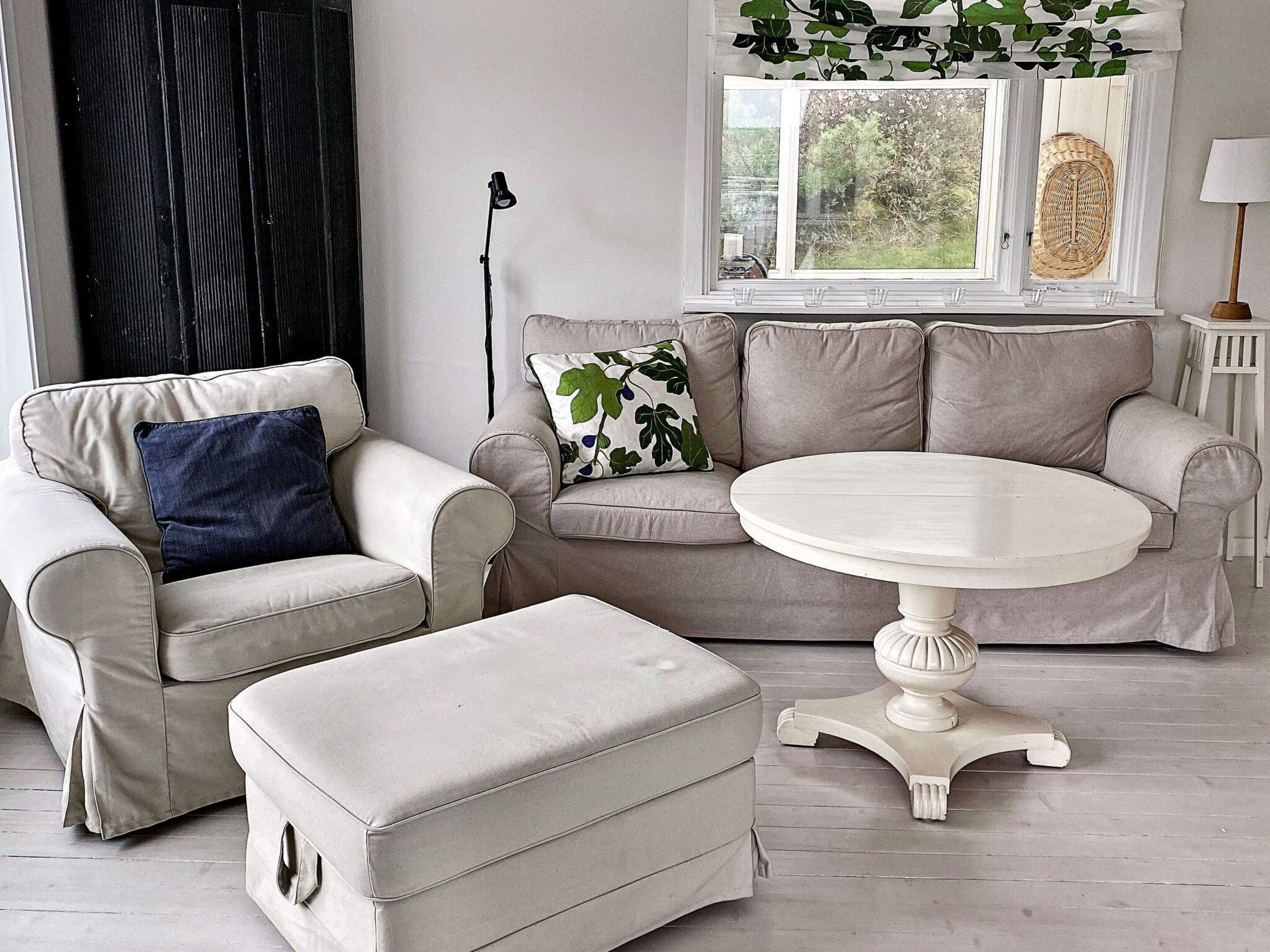 Una sala de estar con un sofá color beige, una mesa redonda blanca y un reposapiés a juego.