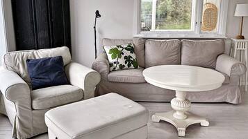 A living room with a beige sofa, a round white table, and a matching ottoman.
