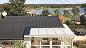Ein Haus mit geneigtem Dach, einem Wintergarten mit Essbereich und Blick auf einen See und einen bewaldeten Bereich.