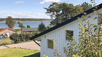 A white cabin with a view of a lake and distant trees.
