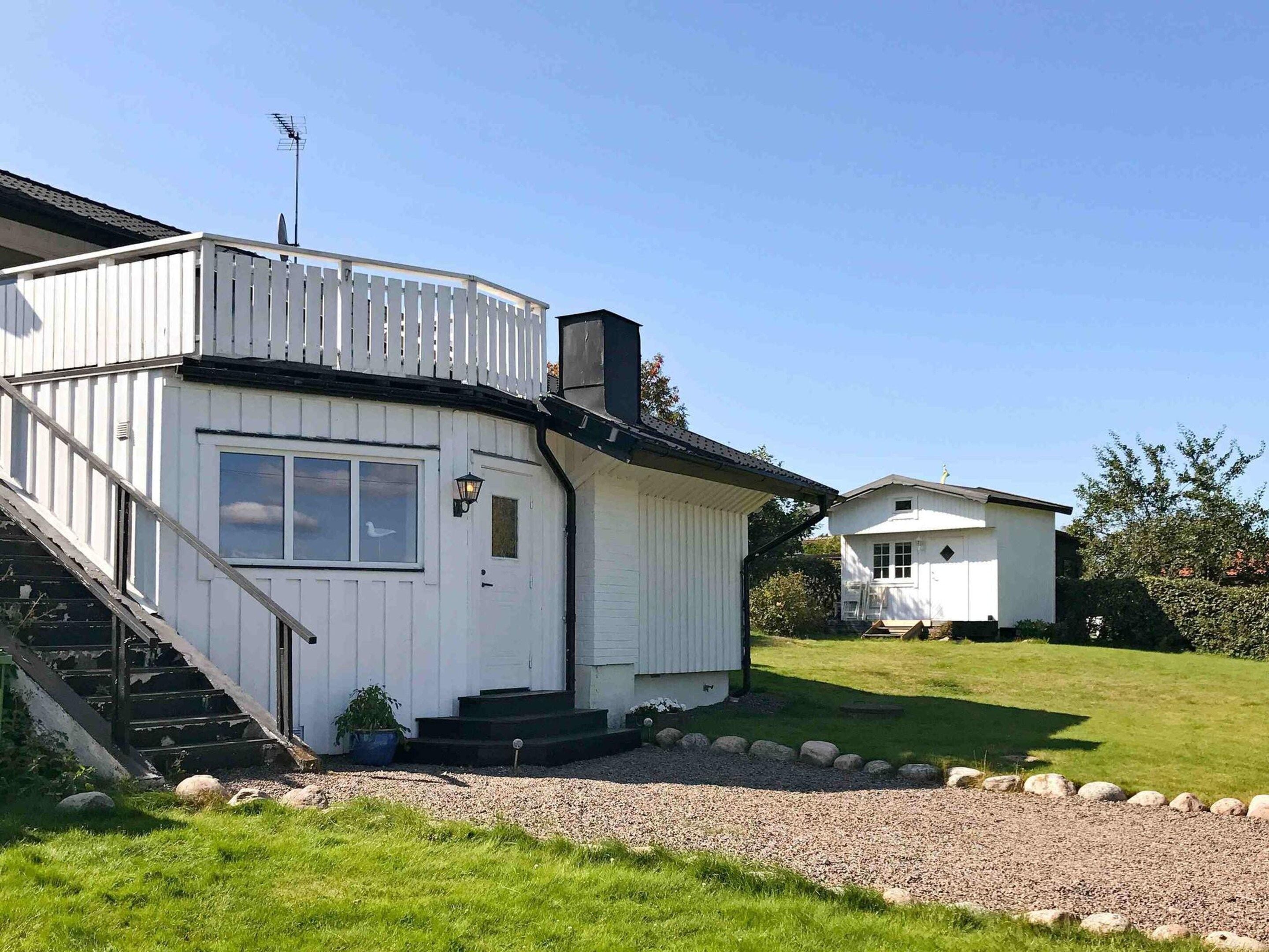 A white two-story house with a balcony, a small attached garage, and a gravel driveway.