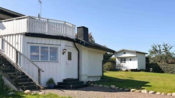 A white two-story house with a balcony, a small attached garage, and a gravel driveway.