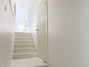 A white interior hallway with a staircase leading to a door. - Holiday Home in Åskloster (Åskloster)