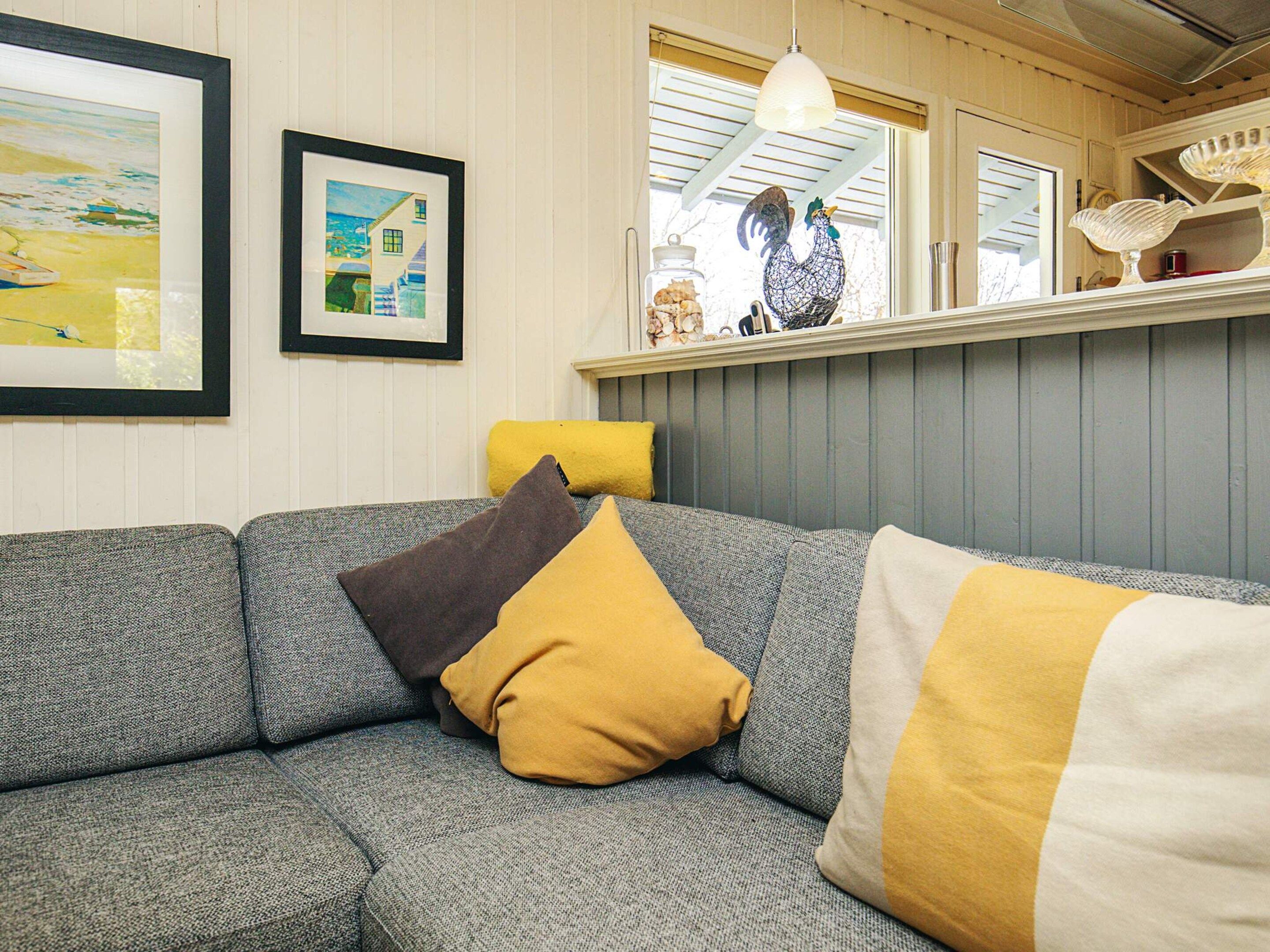 A cozy living room with a grey sofa, yellow and brown cushions, and a decorative rooster on a shelf.