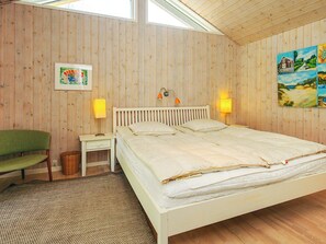 Un dormitorio con una cama nido de madera, dos lámparas de noche, una silla verde, un cuadro enmarcado y un cuadro en la pared.