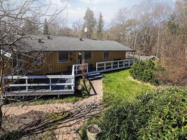 A wooden cabin with a deck, surrounded by trees and a grassy area.