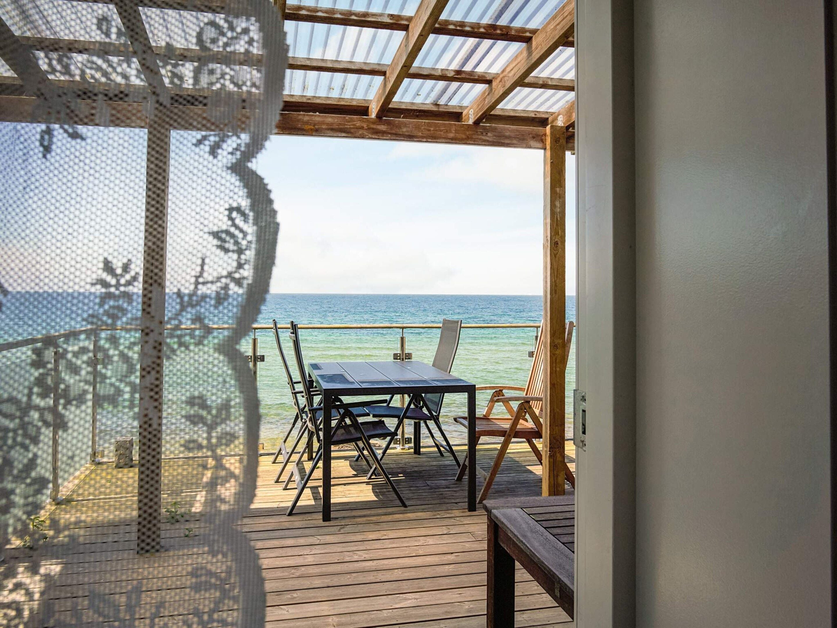 A wooden deck with a table and chairs, overlooking a calm sea.