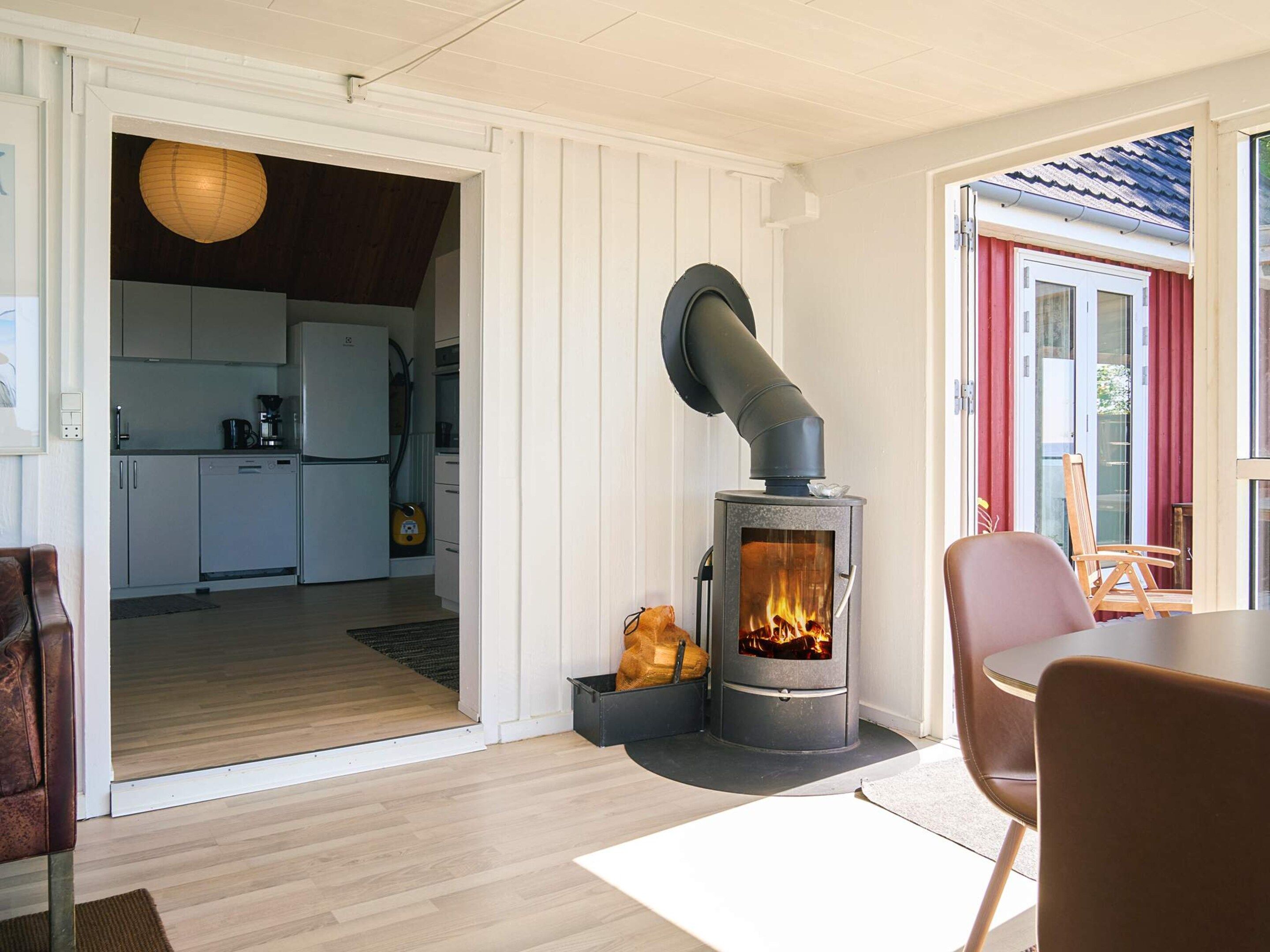 A modern interior with a wood-burning stove, a dining area, and a kitchen visible through an open door.