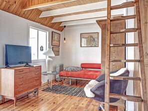 A room with a wooden ceiling, a TV on a wooden cabinet, a red sofa, a small table with a lamp, and a ladder against the wall. - Sunlit Holiday Home in Bornholm near Sea (Ronne)