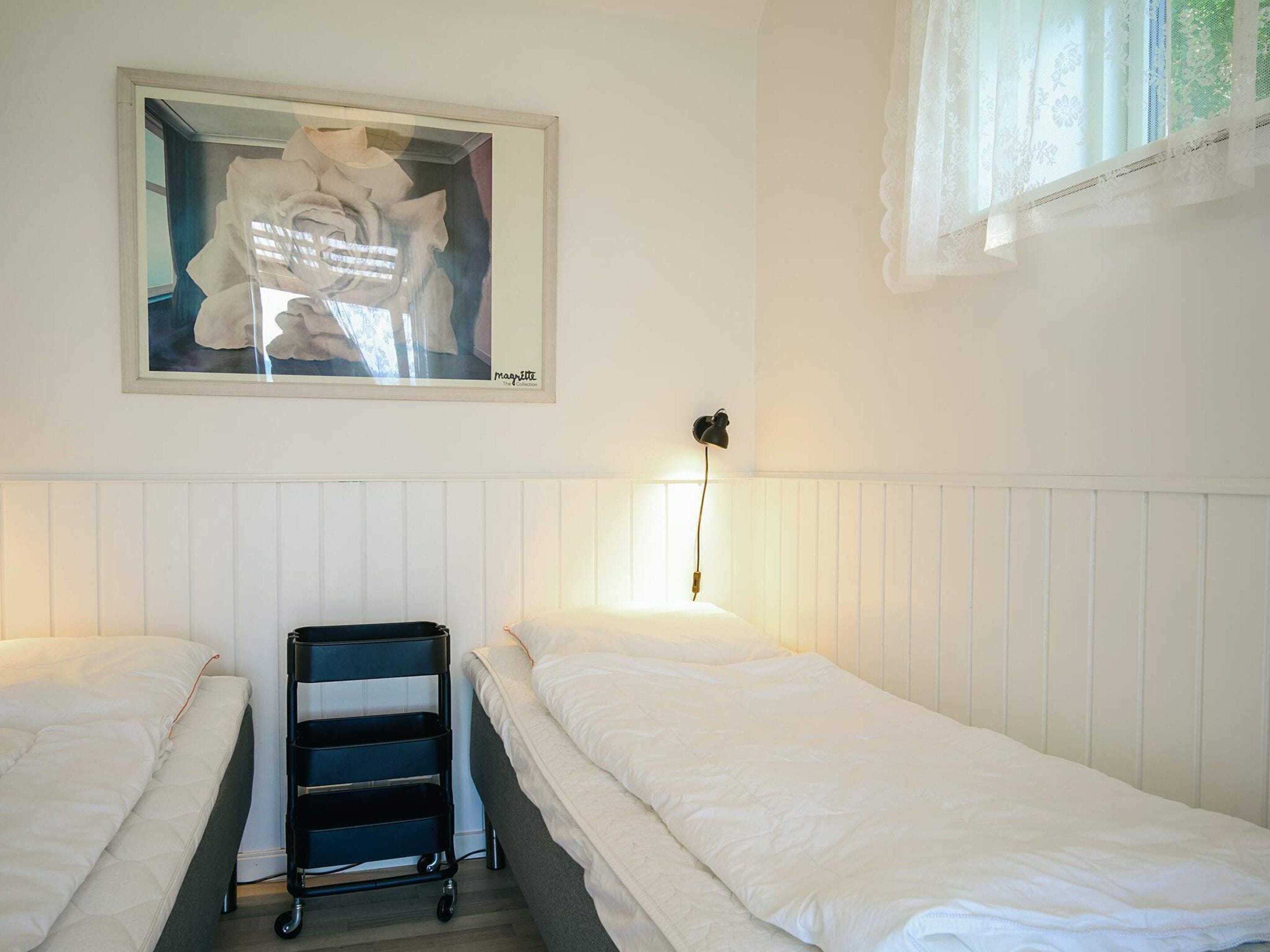 A room with two single beds, a bedside table, a wall-mounted lamp, and a framed artwork above the beds.