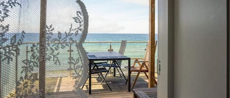 A wooden deck with a table and chairs, overlooking the sea.