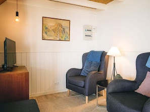 A room with a television on a wooden stand, a framed painting on the wall, a power outlet, and a lamp on a small table. - Sunlit Holiday Home in Bornholm near Sea (Ronne)