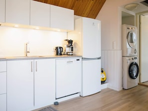 A compact kitchen with white cabinetry, a built-in dishwasher, a coffee maker, and a washing machine. - Sunlit Holiday Home in Bornholm near Sea (Ronne)