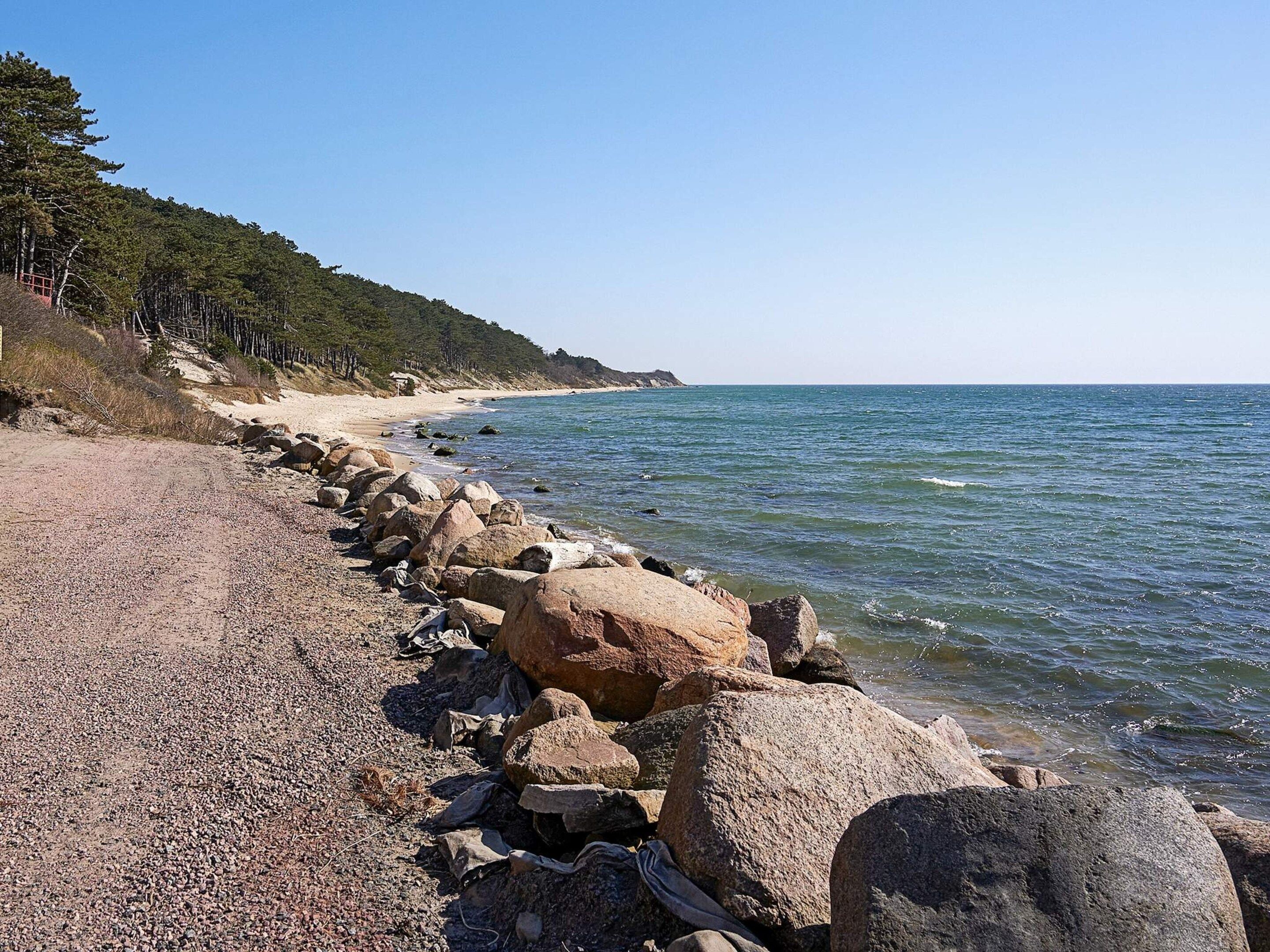 A rocky shoreline with a clear view of the sea and a forested hill in the background.
