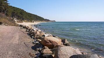 A rocky shoreline with a clear view of the sea and a forested hill in the background.