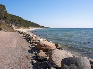 A rocky shoreline with a clear view of the sea and a forested hill in the background. - Sunlit Holiday Home in Bornholm near Sea (Ronne)
