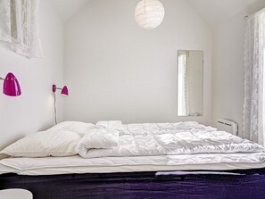 Une chambre à coucher avec un lit, un miroir, un mur blanc et un luminaire au plafond.