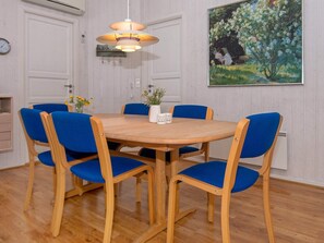 Comedor con mesa de madera, sillas azules, lámpara colgante y un cuadro en la pared.