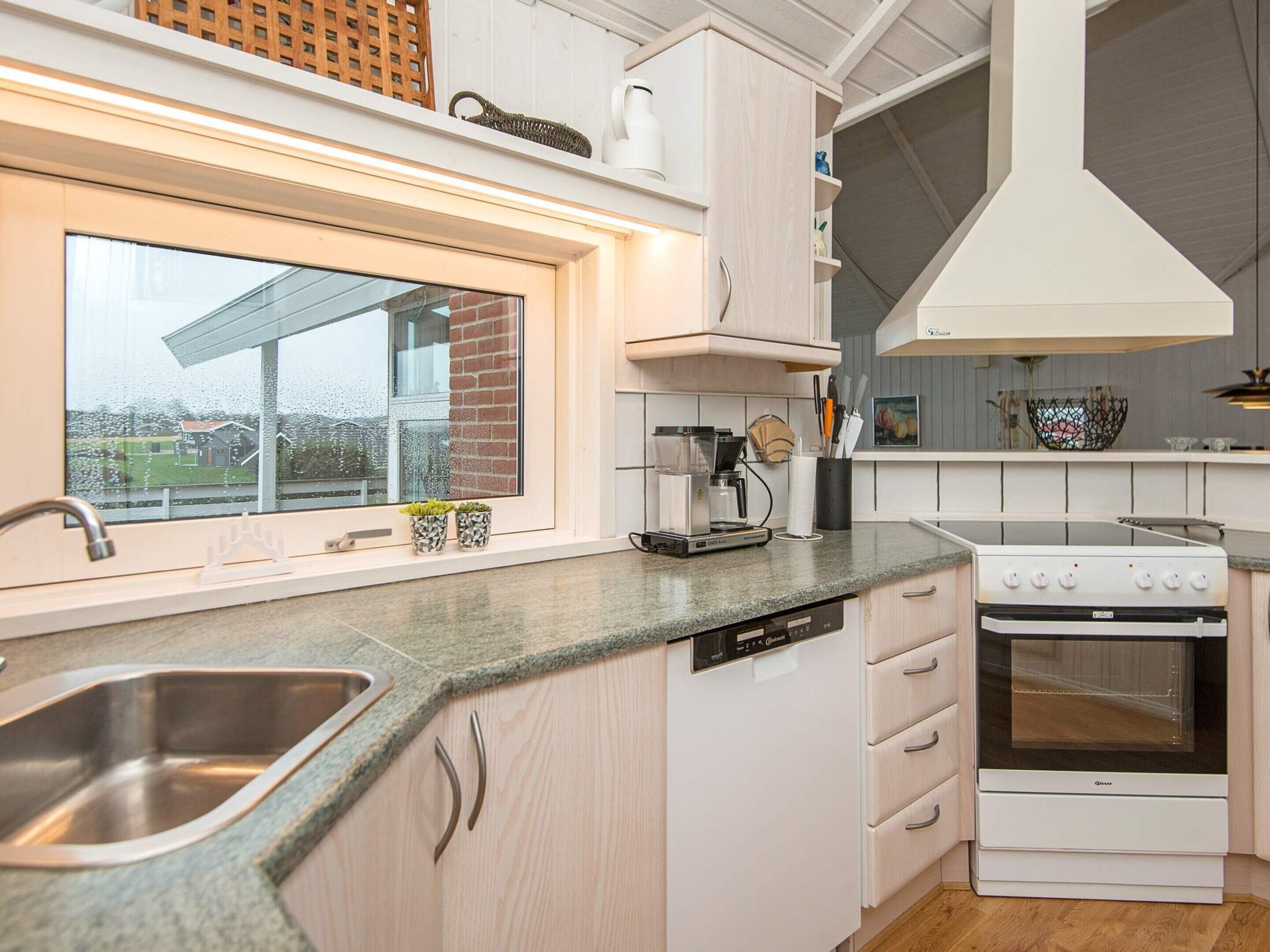 A modern kitchen with a built-in dishwasher, a stove, and a window overlooking a brick house.