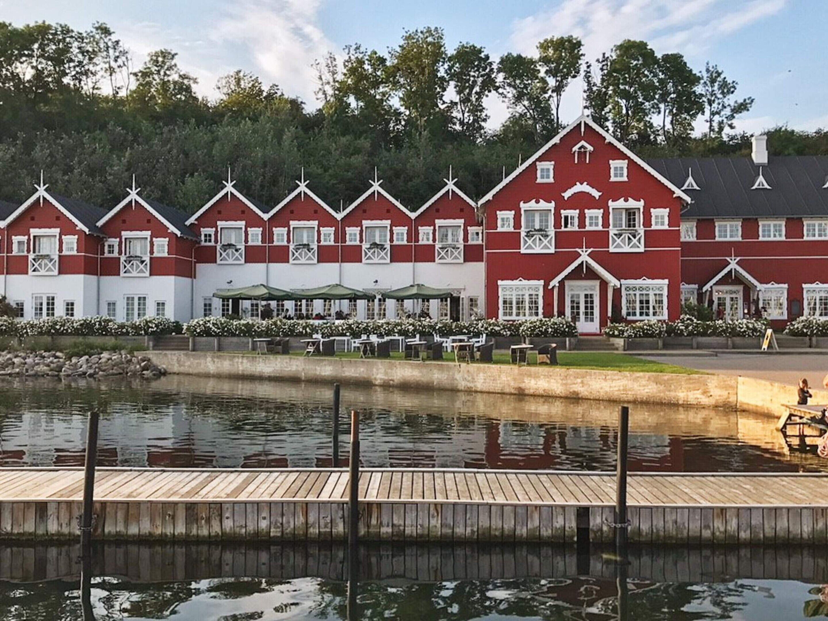 A row of red and white buildings with a dock extending into a calm body of water.