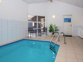 An indoor swimming pool with a metal ladder, a door with a sign, and a potted plant.