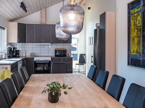 A modern kitchen with dark cabinets, a wooden dining table, and a hanging light fixture. - 5 Star Holiday Home in Logstor (Logstor)