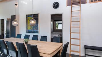 Uma sala de jantar com uma mesa de madeira comprida, cadeiras pretas e luminárias pendentes.