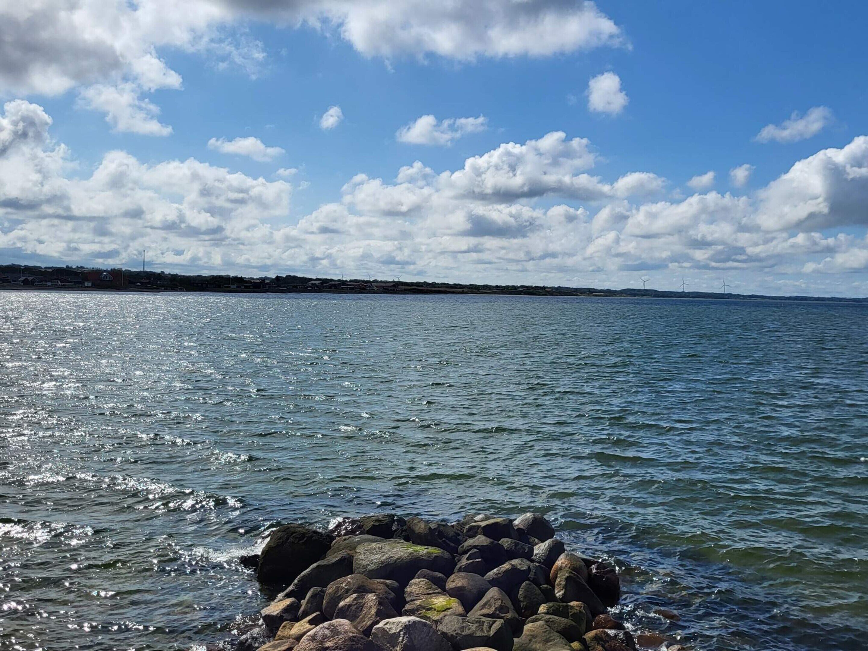 A calm body of water with a rocky shoreline and a distant view of wind turbines.