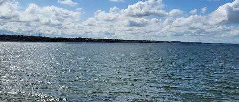 A calm body of water with a rocky shoreline and a distant view of wind turbines.