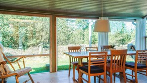 A wooden dining table with chairs, a rocking chair, and a hanging lamp in a room with large windows.