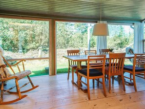 A wooden dining table with chairs, a rocking chair, and a hanging lamp in a room with large windows.