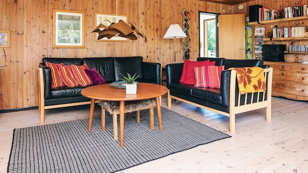 A cozy room with wooden walls, a black leather sofa, a wooden coffee table, and a bookshelf filled with books.