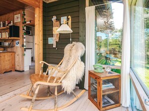 Ein gemütliches Holzinterieur mit einem Schaukelstuhl, einem kleinen Holzschrank mit Glastüren und Blick ins Freie durch ein großes Fenster.