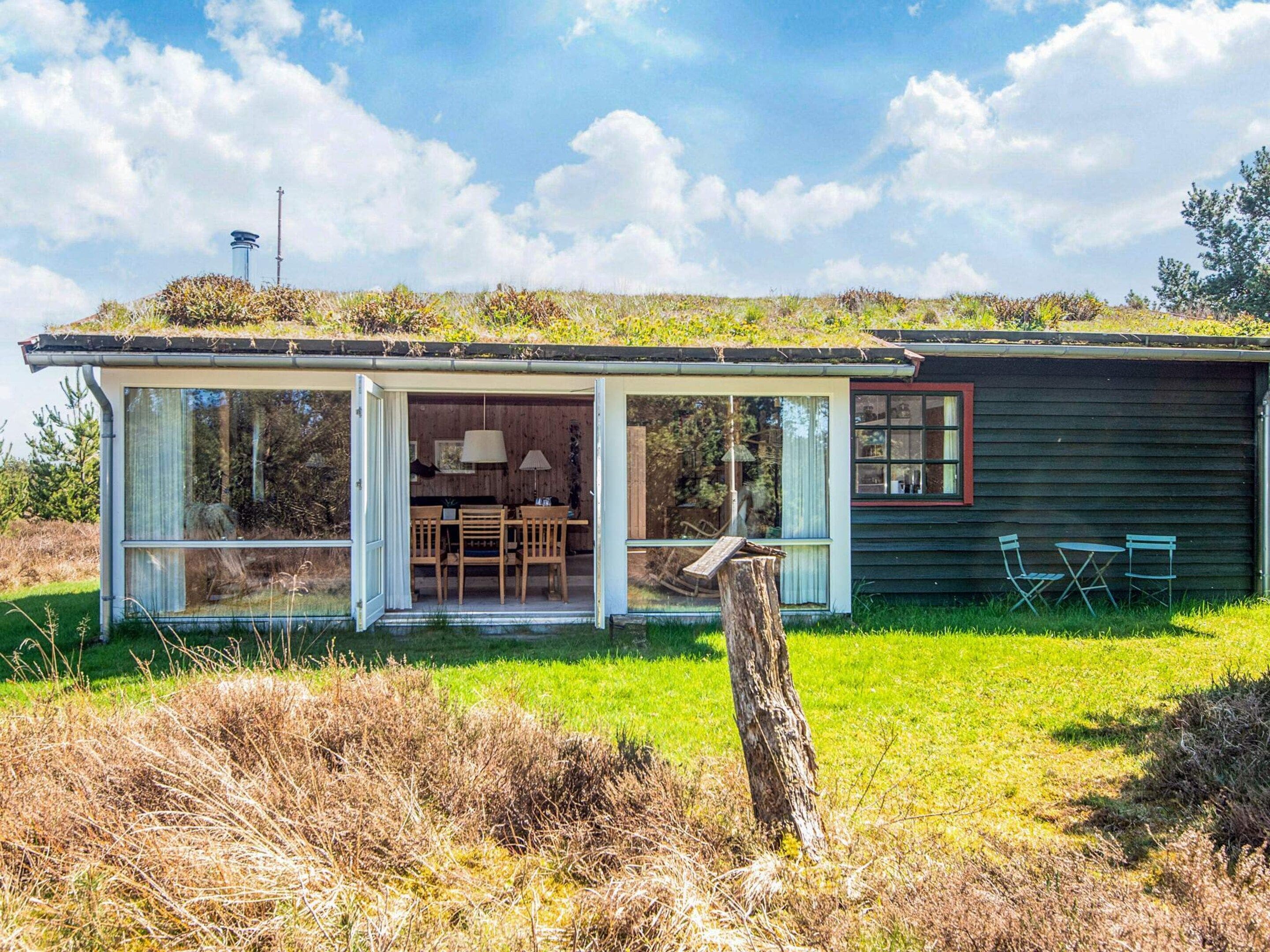 A modern house with a glass-enclosed porch, a dining area with a table and chairs, and a small deck.