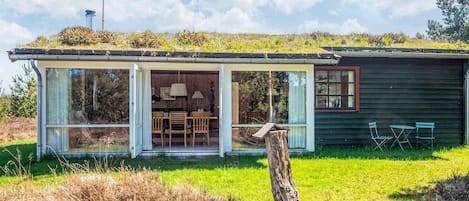Ett modernt hus med en inglasad veranda, en matplats med bord och stolar samt en liten uteplats.