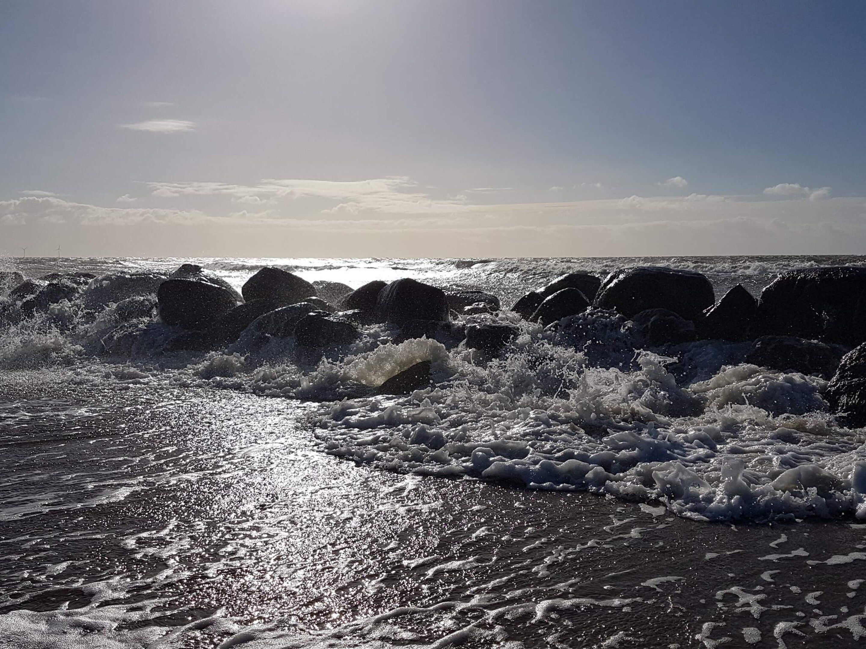 Een strand met golven die tegen rotsen slaan onder een heldere lucht.