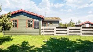 A rustic cabin with a green exterior and red trim, a wooden fence, and a clear sky.