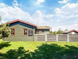 A rustic cabin with a green exterior and red trim, a wooden fence, and a clear sky.