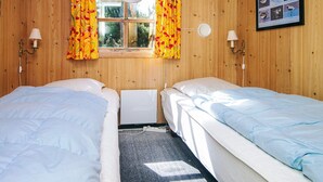 A room with two beds, wooden walls, a window with curtains, a wall-mounted lamp, and a framed bird poster.