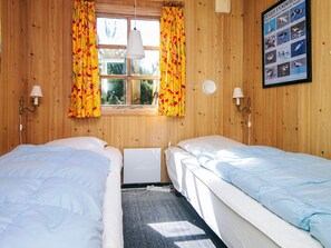 A room with two beds, wooden walls, a window with curtains, a wall-mounted lamp, and a framed bird poster.