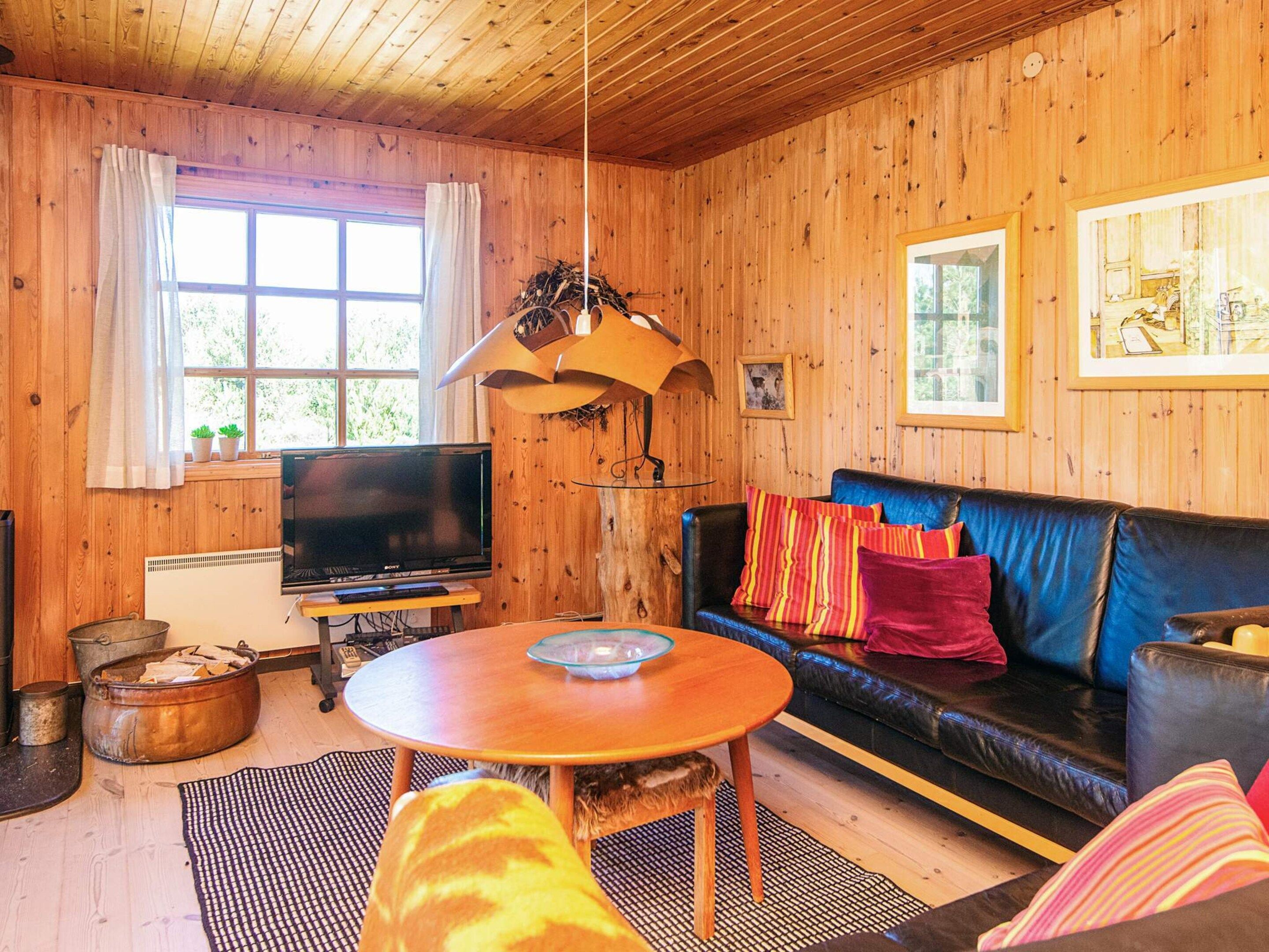 A cozy cabin interior with wooden walls, a black leather sofa, a wooden coffee table, a television, and a fireplace.