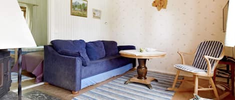 Une pièce avec un canapé bleu, une table ronde, une chaise à rayures et un tapis à motifs.